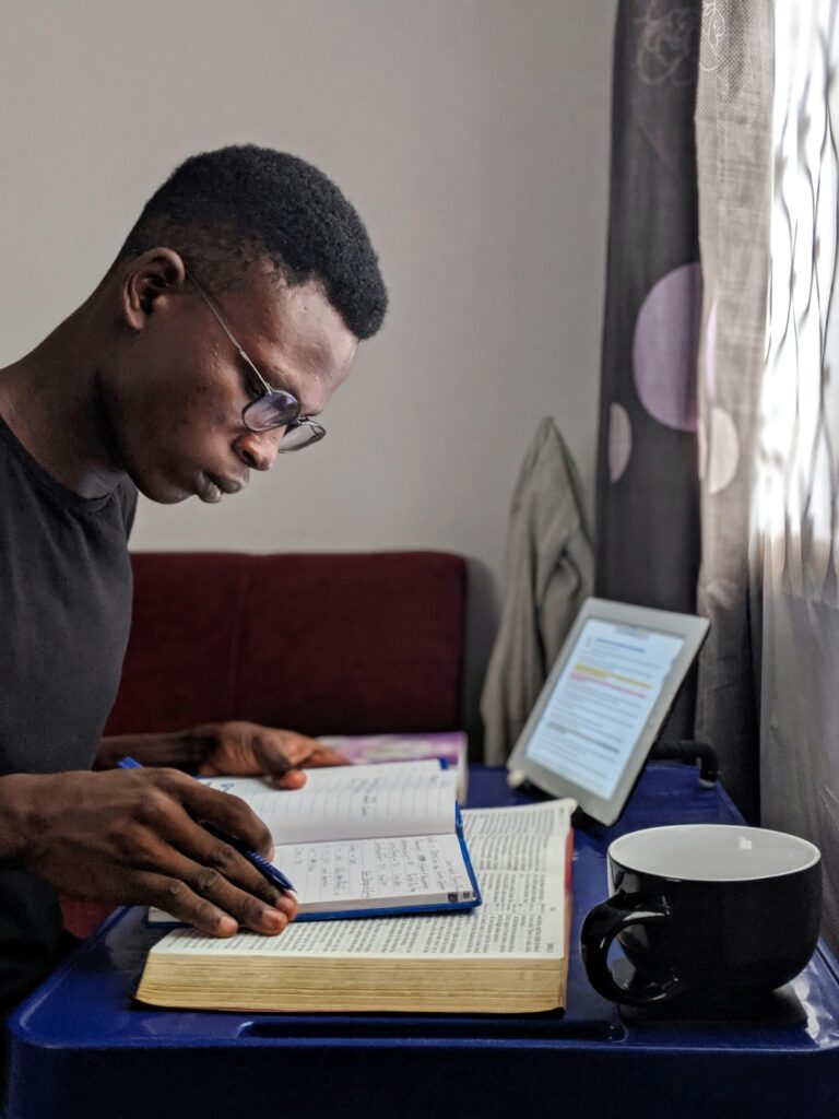 Young man deeply immersed in reading and studying with books and tablet at a comfortable student accommodation