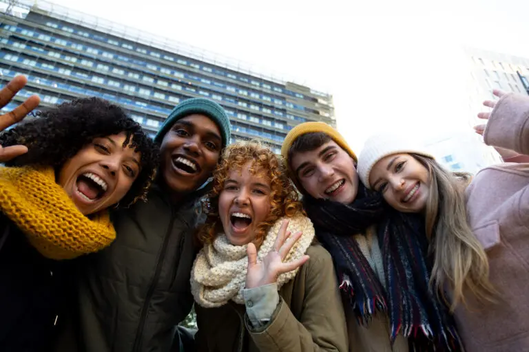 Group of happy multiracial friends looking at camera waving hand and keeping warm in winter time in the city